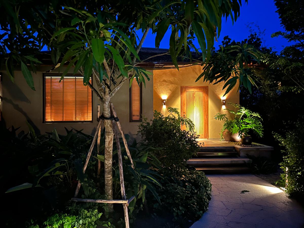 Pool villa entrance lit at twilight with timber doors and stone path, Namia River Retreat, Hoi An, Vietnam