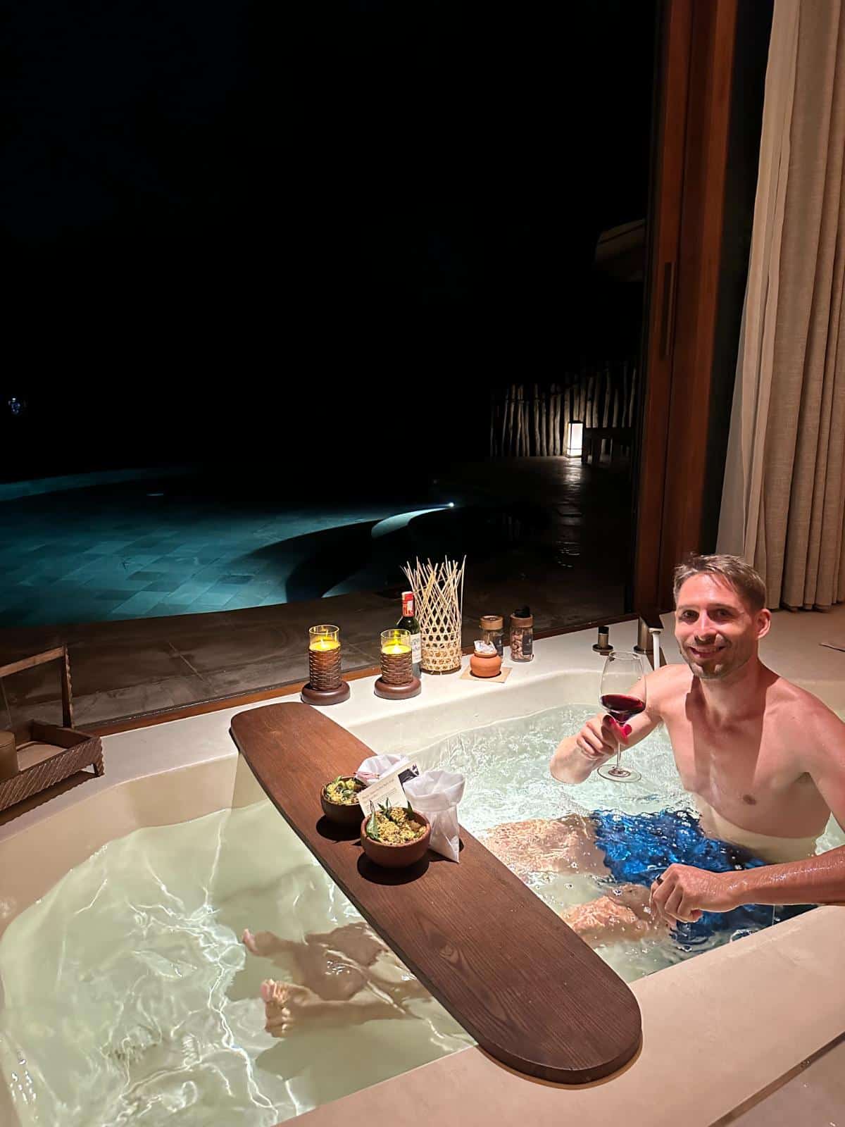 Guest with red wine in the candlelit outdoor jacuzzi at night, Namia River Retreat pool villa, Hoi An, Vietnam