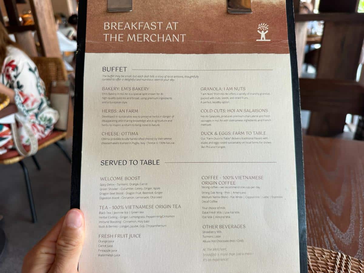 Guest reading The Merchant restaurant breakfast menu, Namia River Retreat, Hoi An, Vietnam