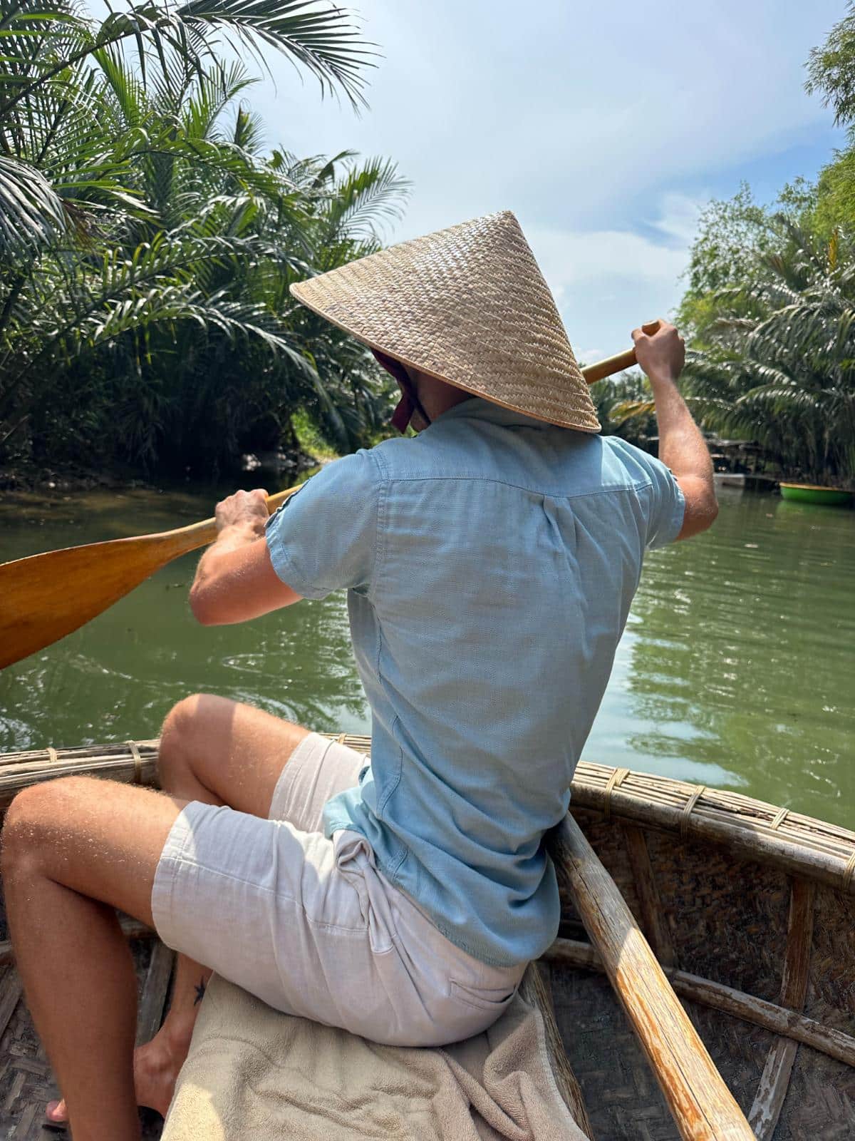 Paddler in a conical hat steers a basket boat through the palm waterway, Namia River Retreat, Hoi An, Vietnam