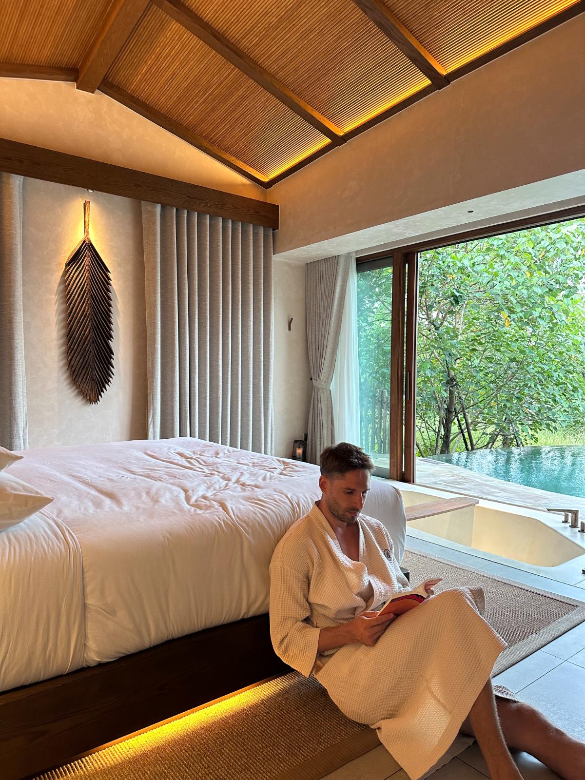 Reading on the bed by floor-to-ceiling pool view window, private pool villa, Namia River Retreat, Hoi An, Vietnam